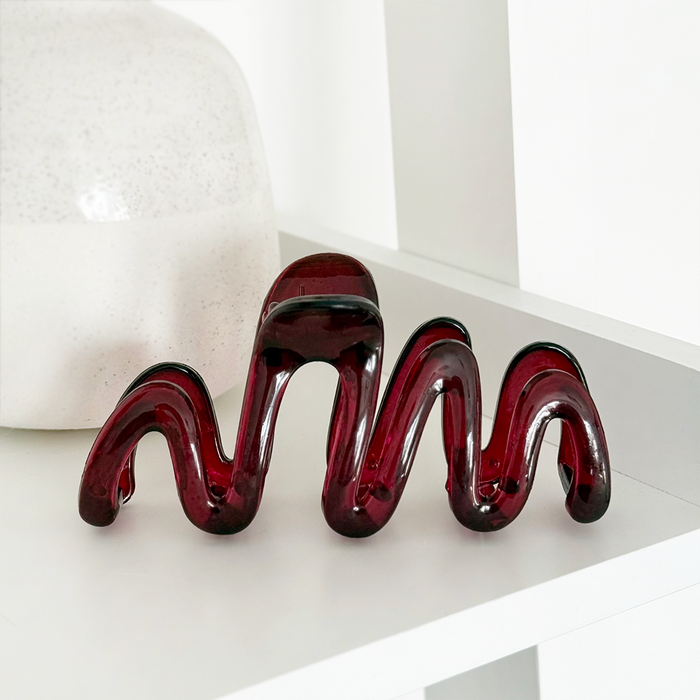 Burgundy squiggle claw clip sits on a white shelf next to a large white ceramic vase.