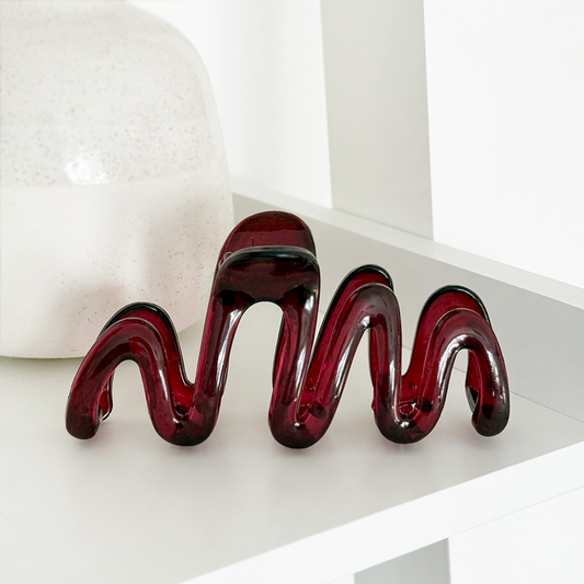 Burgundy squiggle claw clip sits on a white shelf next to a large white ceramic vase.