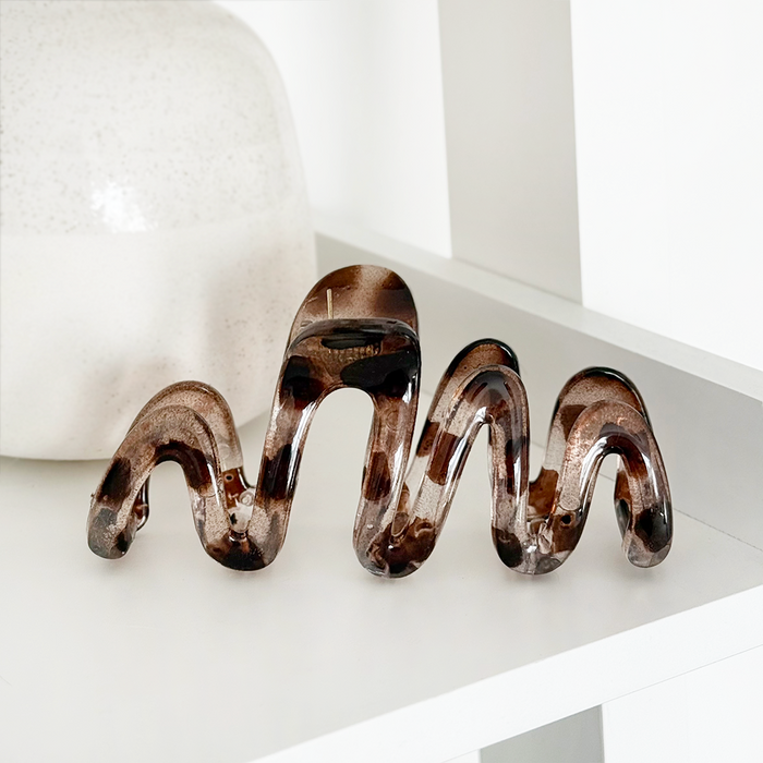 Ivory tortoiseshell squiggle claw clip by Coconut Lane on a white shelf next to a round ceramic vase.