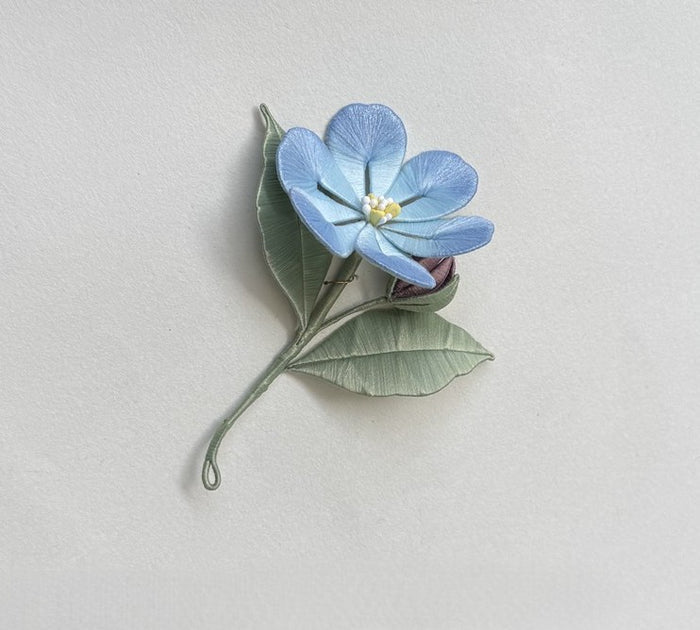 Finished silk-wrapped blue Statice flower with a purple bud and green leaves, laid flat, a handmade DIY flower project.