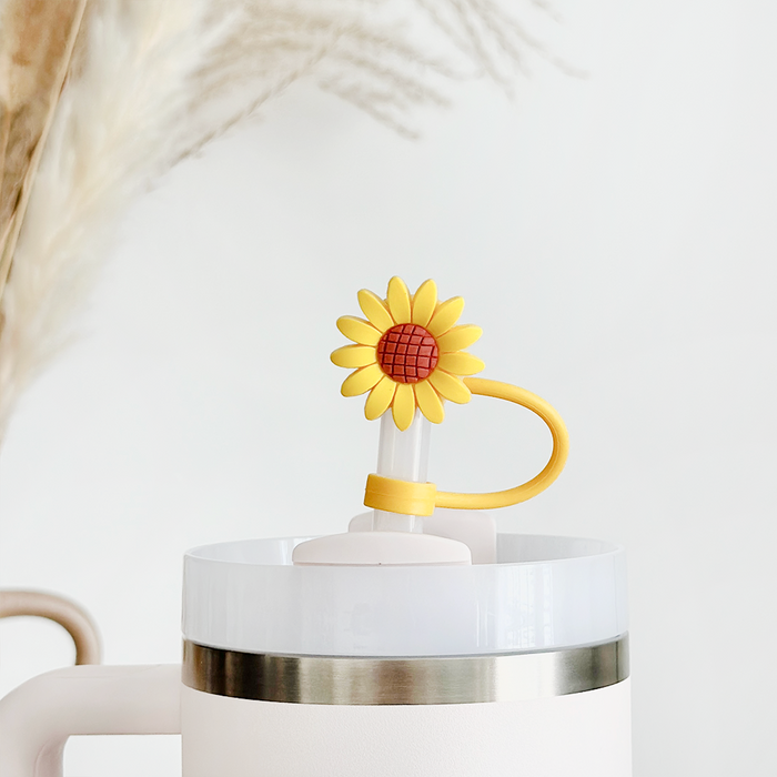 White tumbler with handle featuring a sunflower straw cover, placed in front of dried pampas grass.