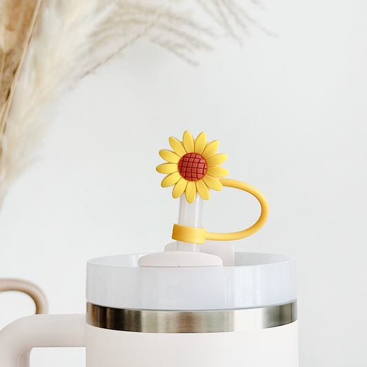 White tumbler with handle featuring a sunflower straw cover, placed in front of dried pampas grass.
