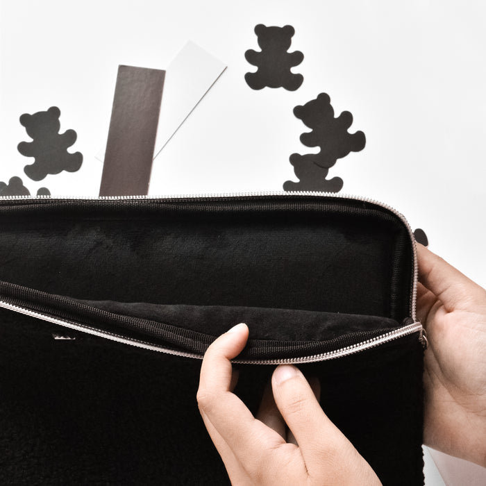 Hands opening a Coconut Lane Teddy Baloo laptop sleeve with black bear cutouts, on a white surface.