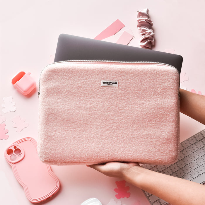 Hands holding a pink Teddy Love-a-Lot laptop sleeve with teddy bear pattern above a laptop on a pink desk.