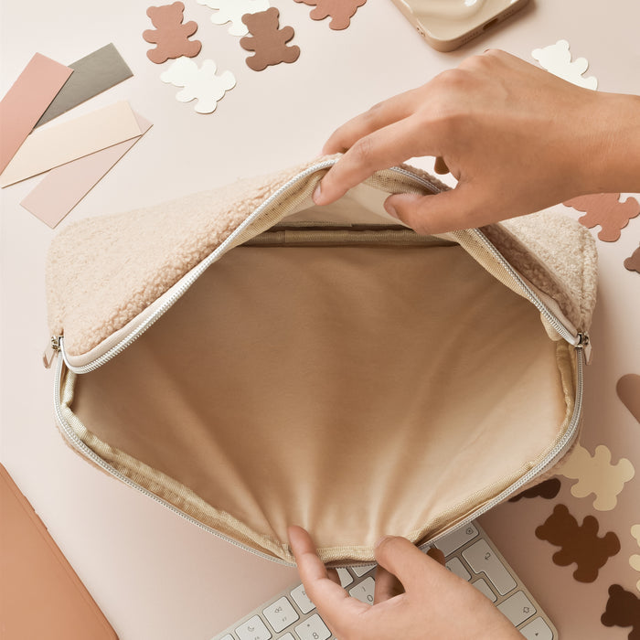 Hands opening a beige Teddy Rupert laptop sleeve on a pastel desk, with color swatches and keyboard next to it.