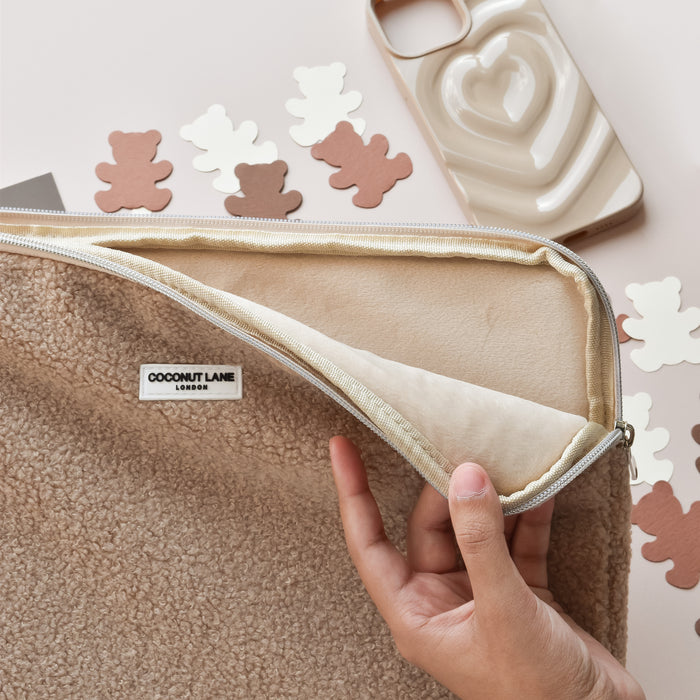 Beige fleece-lined Coconut Lane Teddy Rupert laptop sleeve being opened by a hand on a desk with bear cutouts nearby.