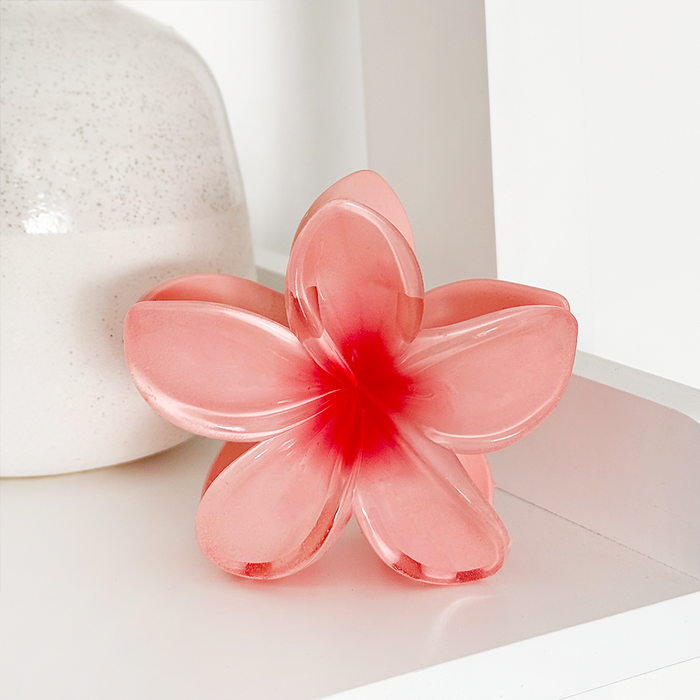 Coral tropical flower-shaped claw clip on a white shelf beside a speckled ceramic vase.