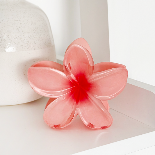 Coral tropical flower-shaped claw clip on a white shelf beside a speckled ceramic vase.