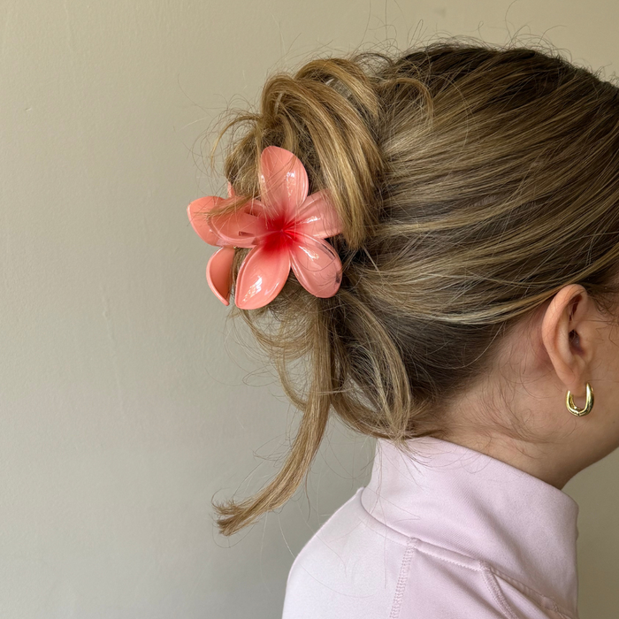 Blonde woman with an updo wears a coral floral claw clip, light pink top, and gold hoop earrings.