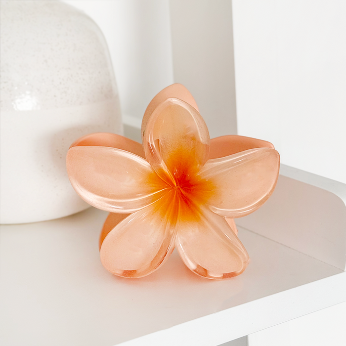 Pink and orange hibiscus flower claw clip by Coconut Lane on a white shelf next to a white vase.