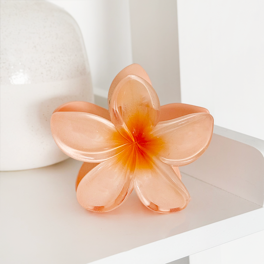 Pink and orange hibiscus flower claw clip by Coconut Lane on a white shelf next to a white vase.