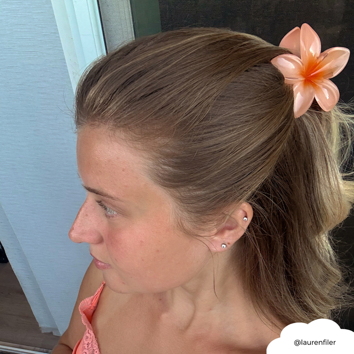 Woman with light brown hair wears a peach top and a Coconut Lane hibiscus-patterned claw clip, facing left.