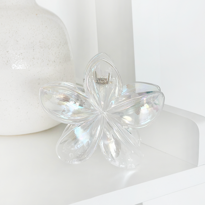 Iridescent glass flower decor next to a clear holographic tropical flower hair claw clip on a white shelf.