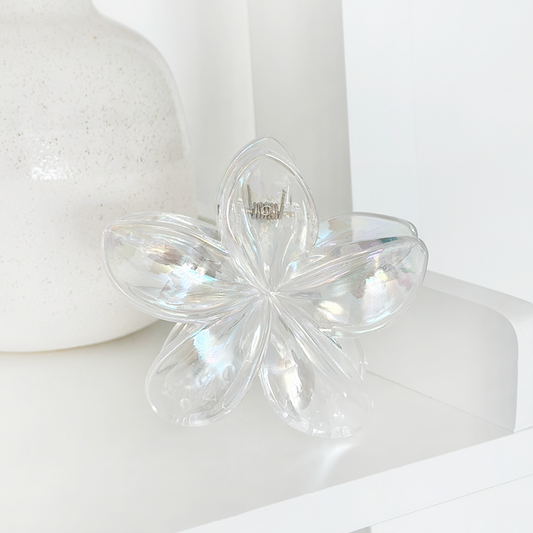 Iridescent glass flower decor next to a clear holographic tropical flower hair claw clip on a white shelf.