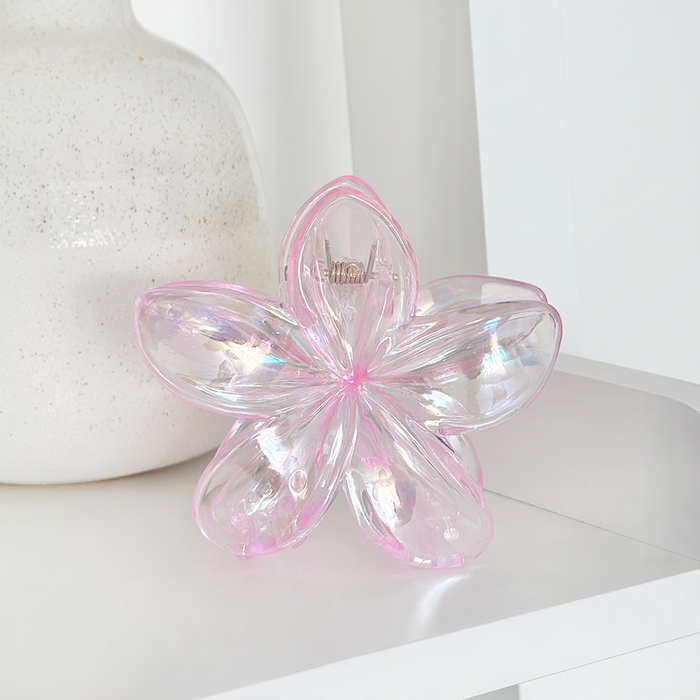 Holographic pink Tropical Flower Claw Clip by Coconut Lane on a white shelf next to iridescent glass and white vase.