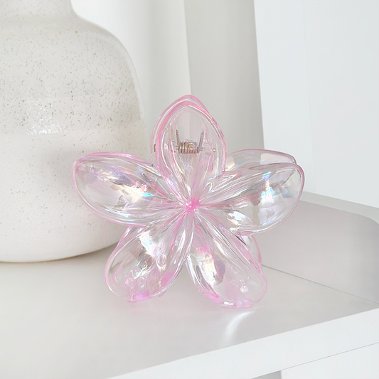 Holographic pink Tropical Flower Claw Clip by Coconut Lane on a white shelf next to iridescent glass and white vase.