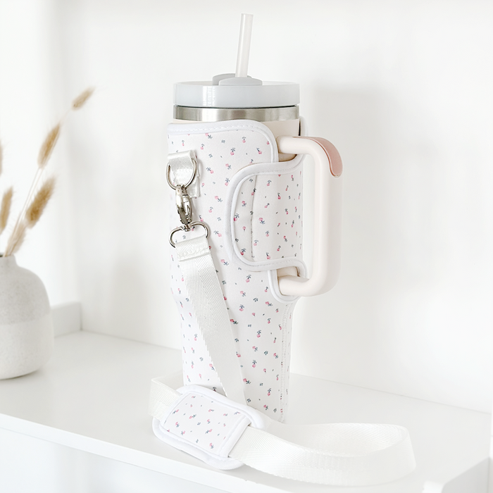 White carry case with ditsy floral pattern and white strap, holding an insulated tumbler with a straw.