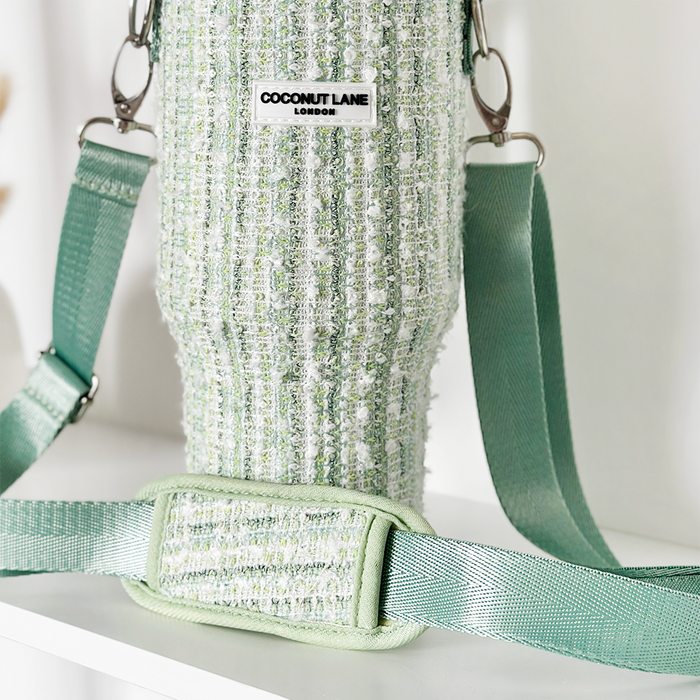 Green textured tweed tumbler carry case with adjustable strap on a white shelf.