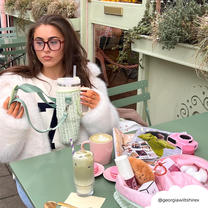 Woman with long brown hair and glasses at a cafe table with a green tweed Coconut Lane tumbler carry case.