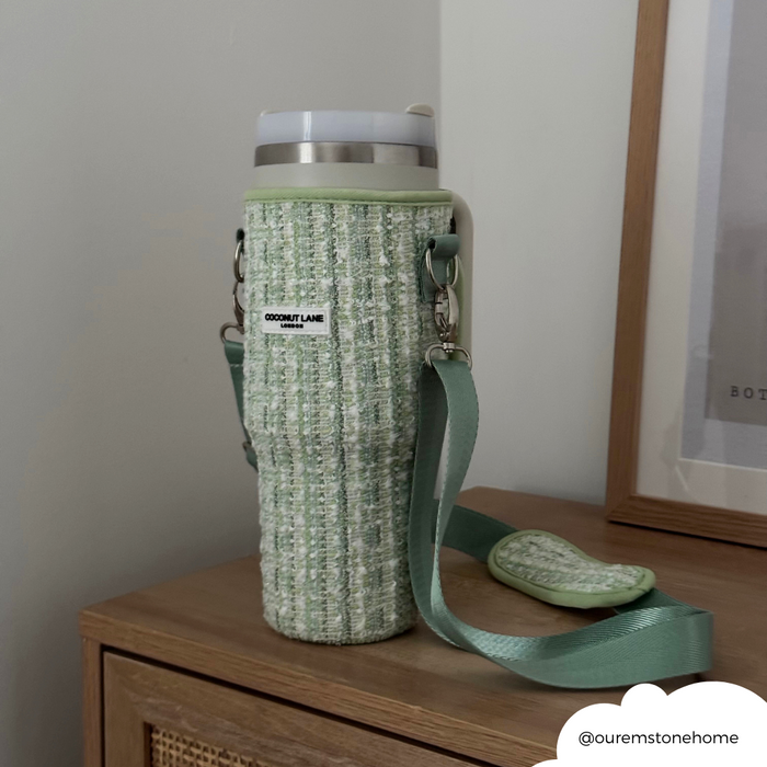 Green tweed tumbler carry case with strap on a wooden cabinet next to a photo frame.