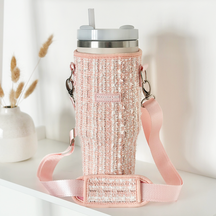 Pink textured tweed tumbler carry case next to a white vase with dried flowers on a shelf.