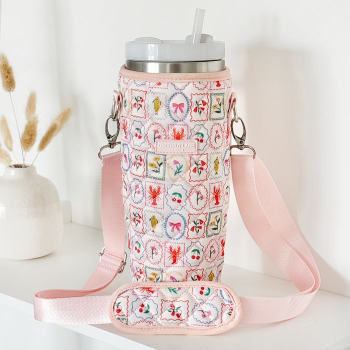 Quilted Dolce Vita Coconut Lane tumbler carry case on a shelf beside a vase of dried flowers.