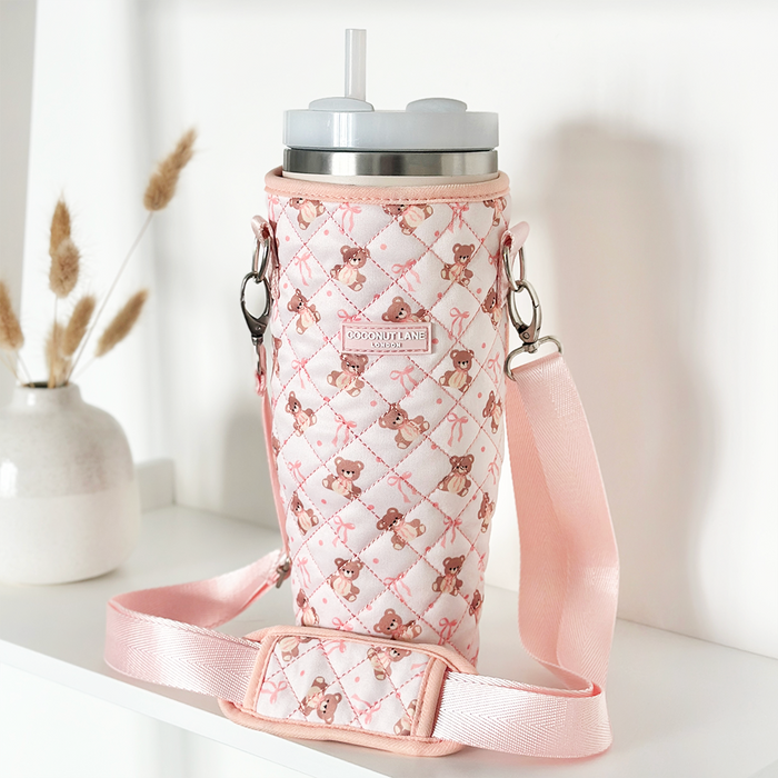 Quilted beige Teddy tumbler carry case with strap on a white shelf next to a vase of dried grass.