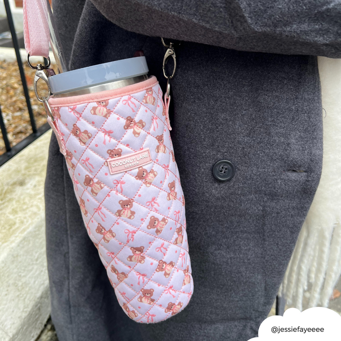 Person in dark coat holding a drink in a beige quilted tumbler carry case with strap by Coconut Lane.