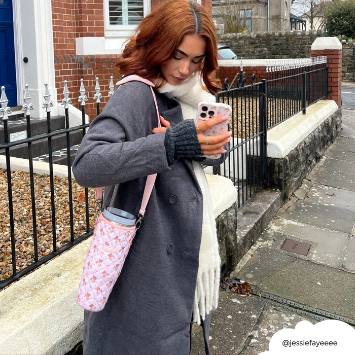 Woman in gray coat checks phone, holding a beige quilted Coconut Lane tumbler carry case with teddy texture.