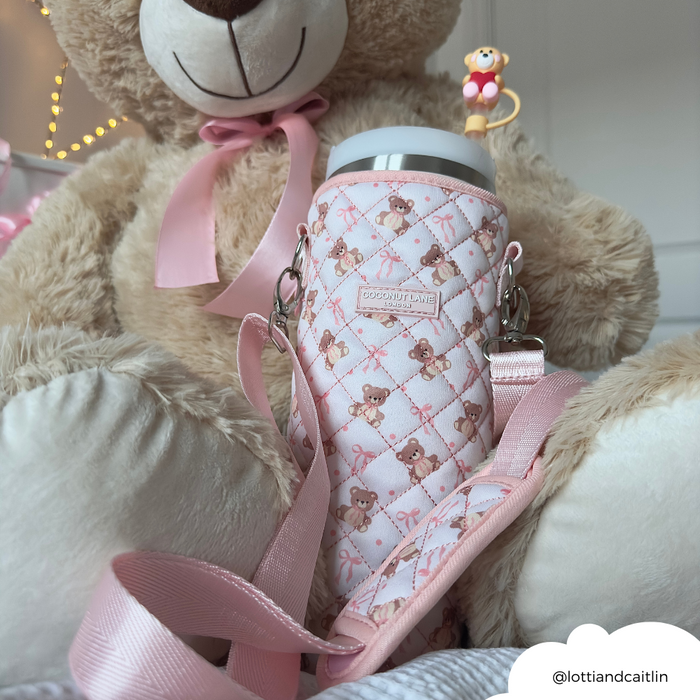 Quilted tumbler carry case with teddy bear print and crossbody strap next to a plush teddy bear.