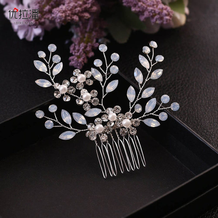 A decorative hair comb with pearl-like beads and crystal flowers, branch design, in a black box, lilac flowers softly blurred behind.